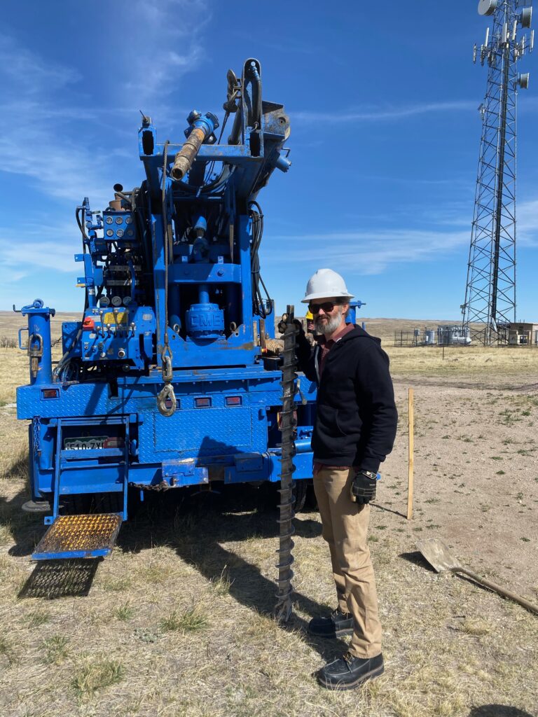 JB Engineers employee standing by some machinery holding a large ground drill bit